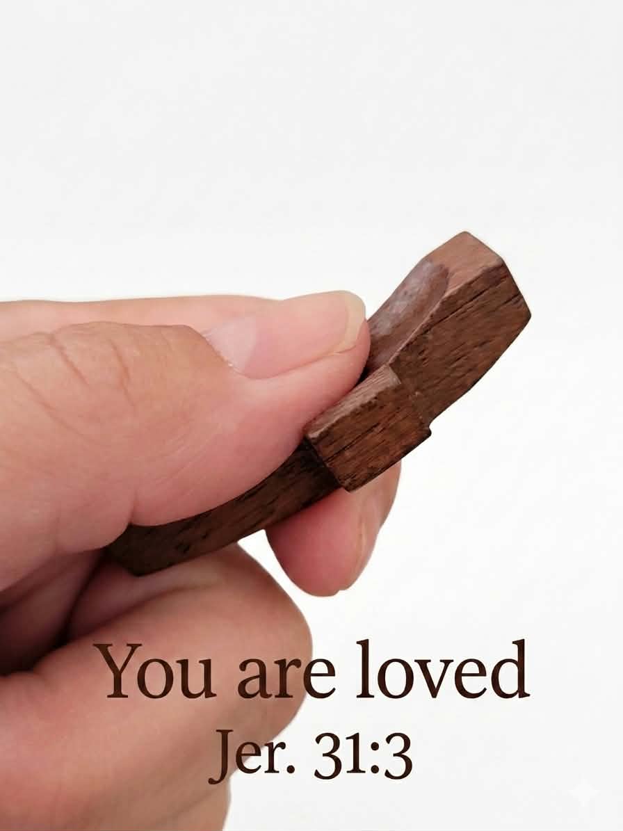 Hand holding wooden thumb cross engraved with You are Loved and Jer. 31:3